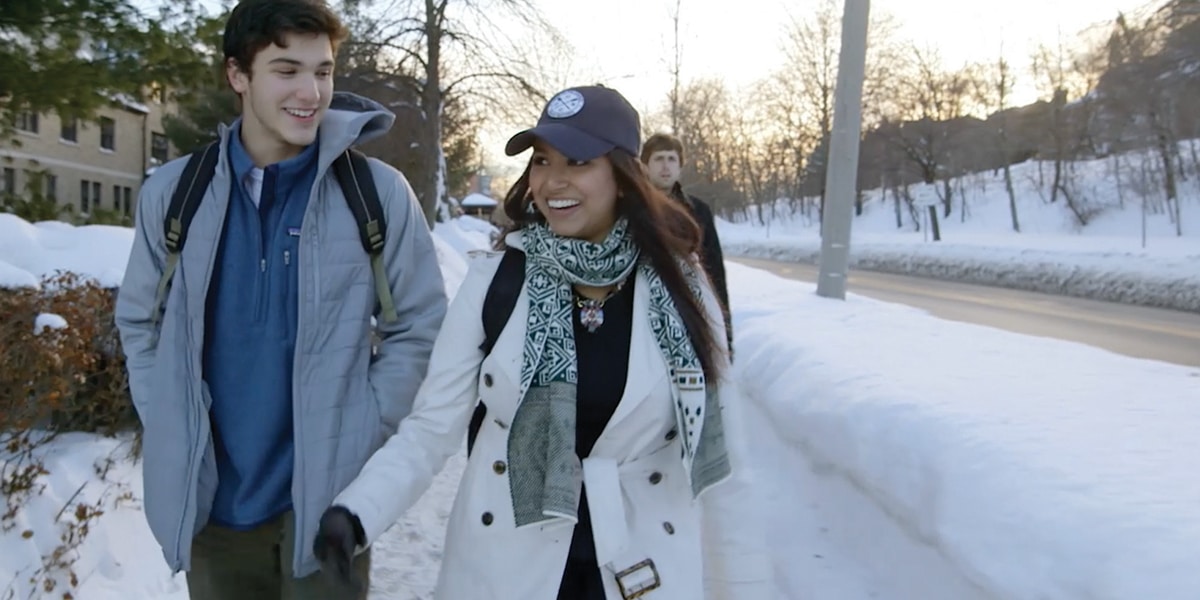 a woman in a white coat and a man in a cap walking in the snow