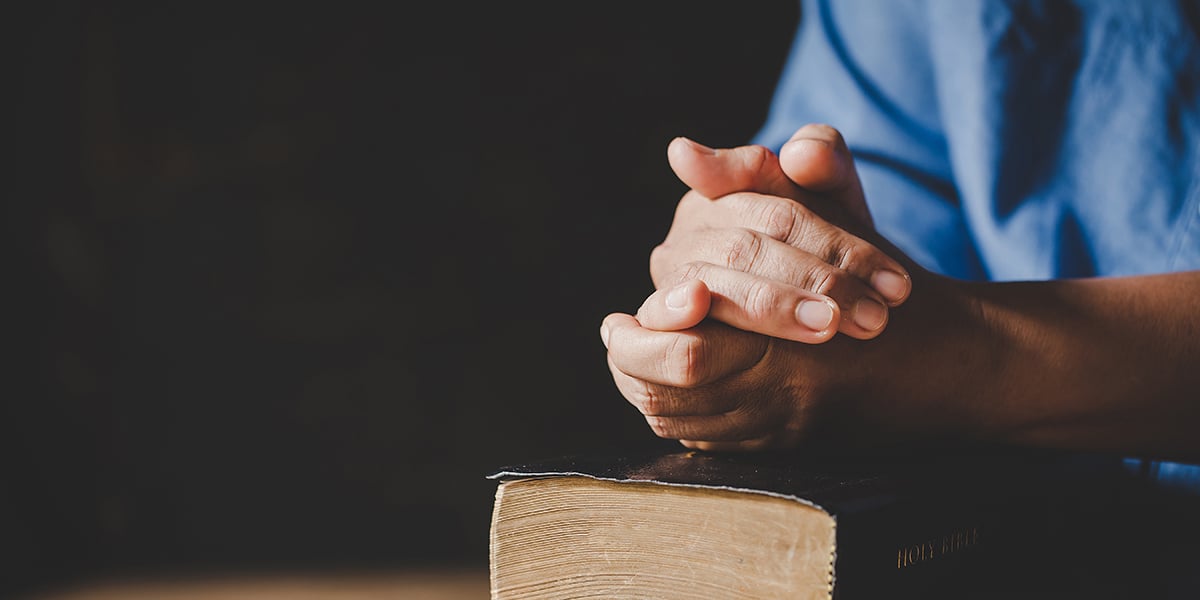 hands folded in prayer over a Bible
