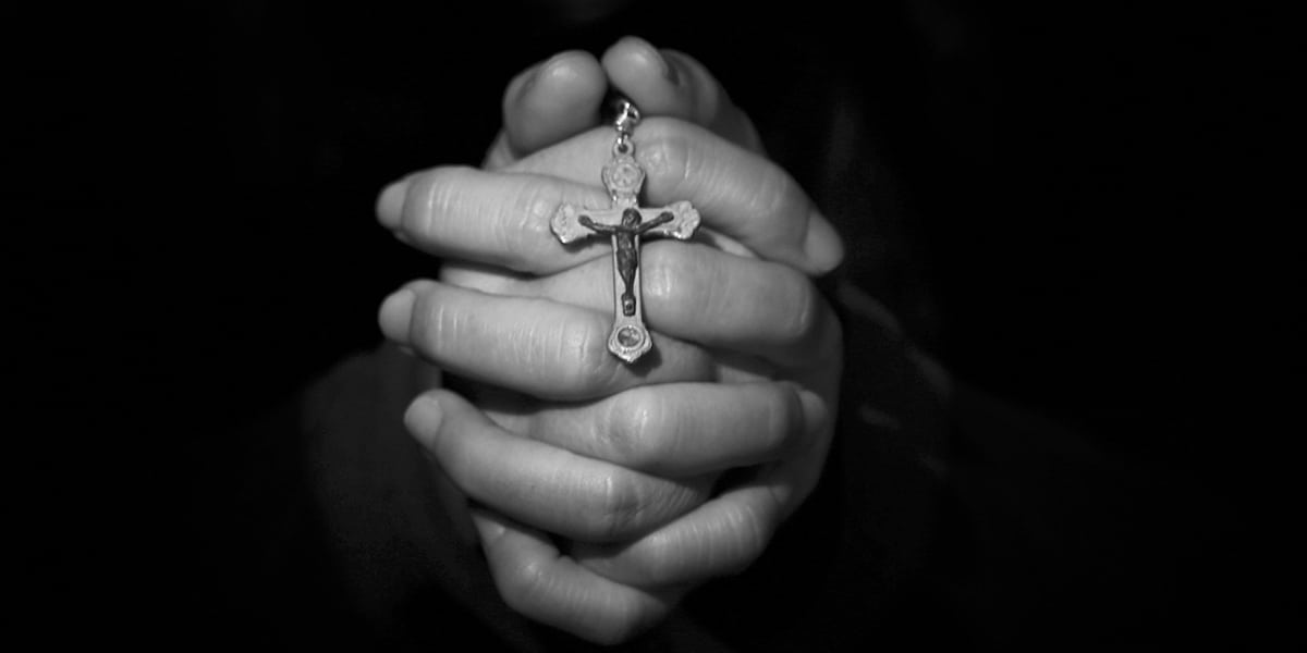 hands folded in prayer while holding a rosary