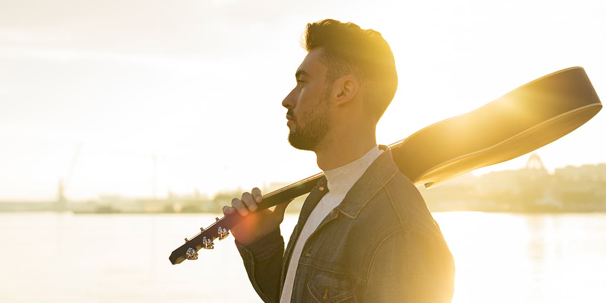 A man holding a guitar while looking into the sunset.
