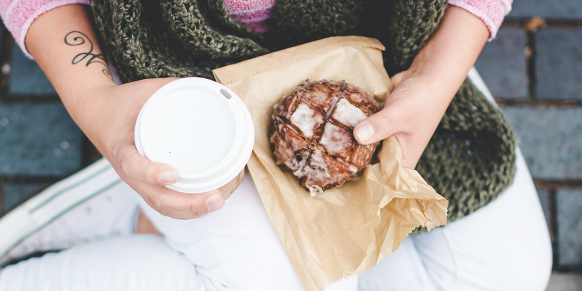 woman holding a coffee and a donut