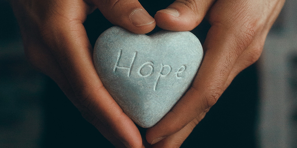 hands holding a stone heart with the word hope carved in it