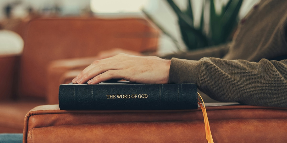 man resting hand on Bible while sitting in a chair