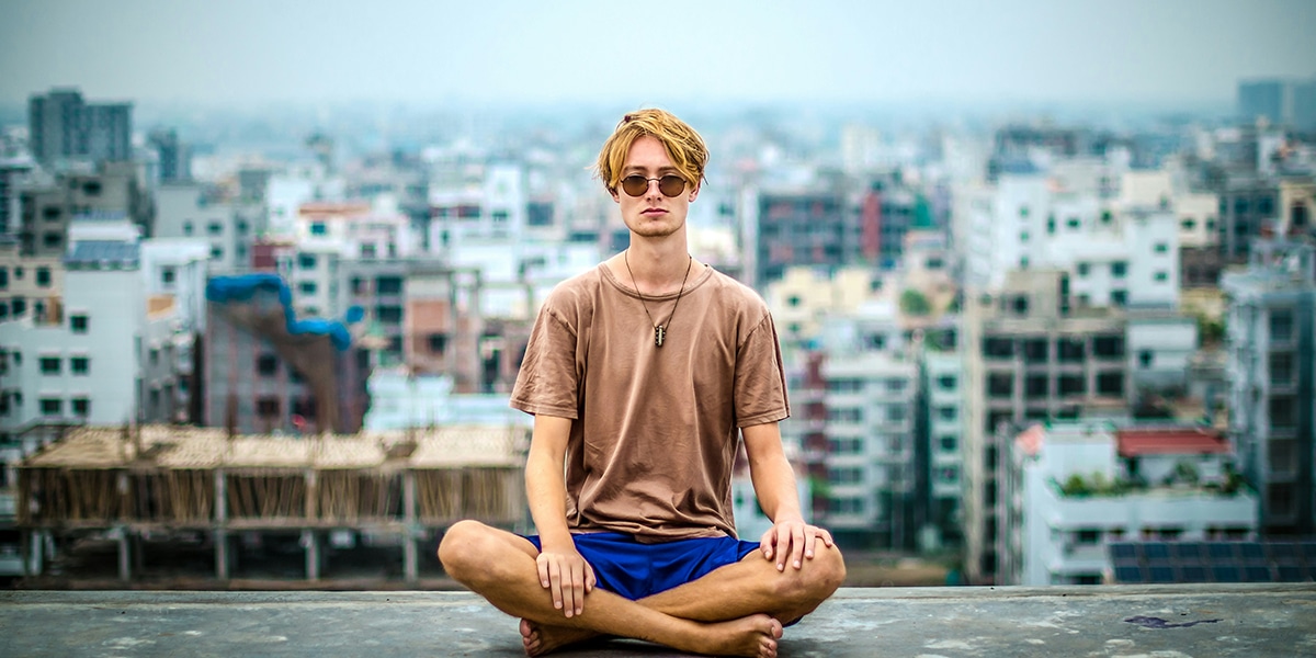 man sitting on a wall meditating with a city in the background