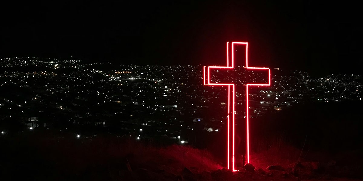 a light up cross at night with a city in the background