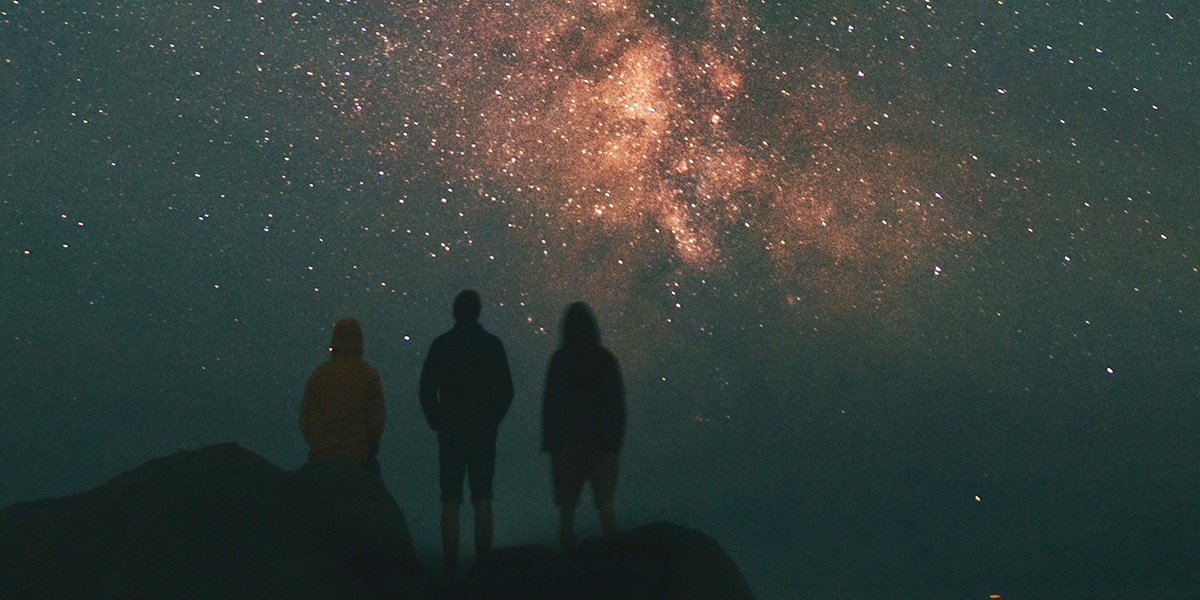Three people are looking at stars in the mountains