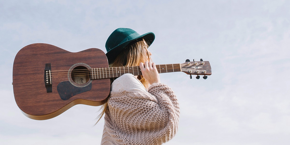 woman wearing a green hat, holding a guitar and carrying it over her shoulder