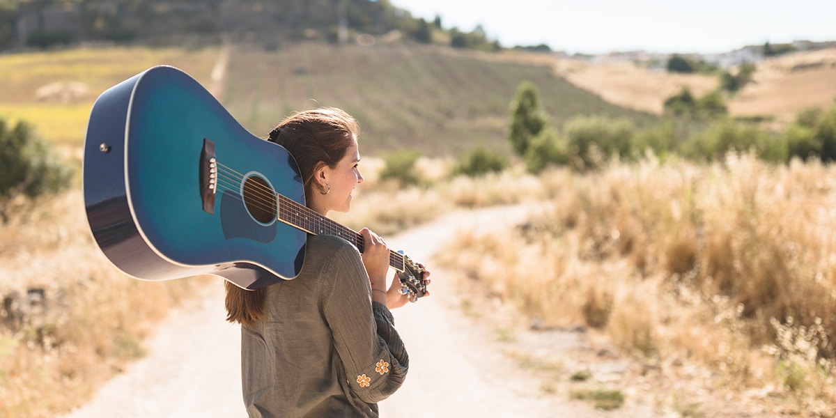 woman carrying a guitar while walking down a road