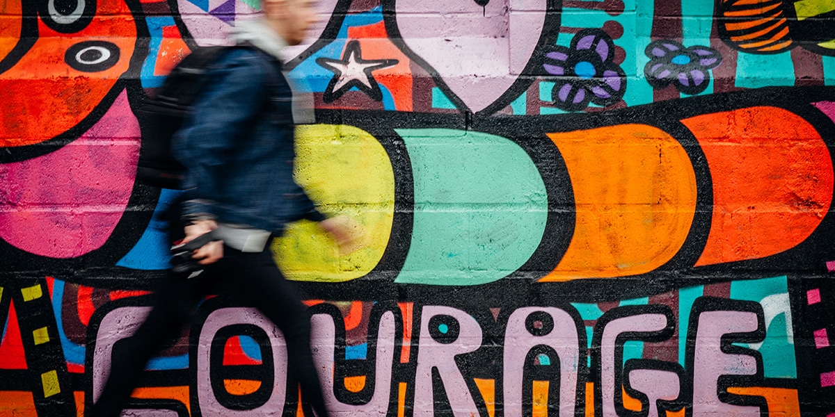 man walking past a wall full of graffiti with the word courage sprayed on it,