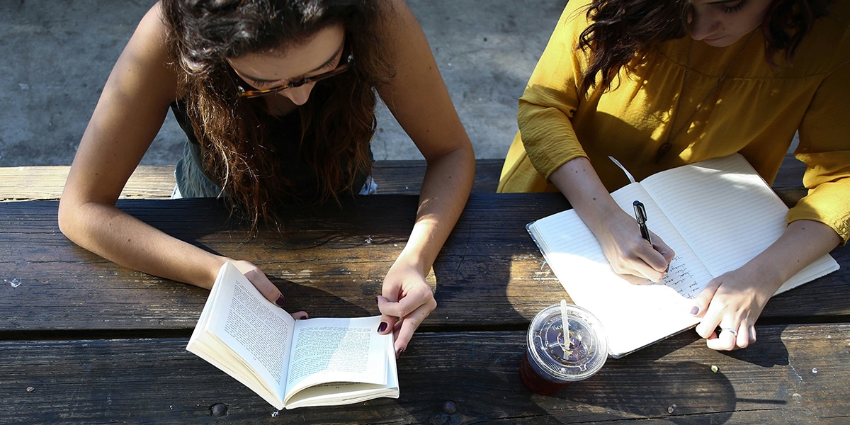 two women writing, discussing while writing in a notebook