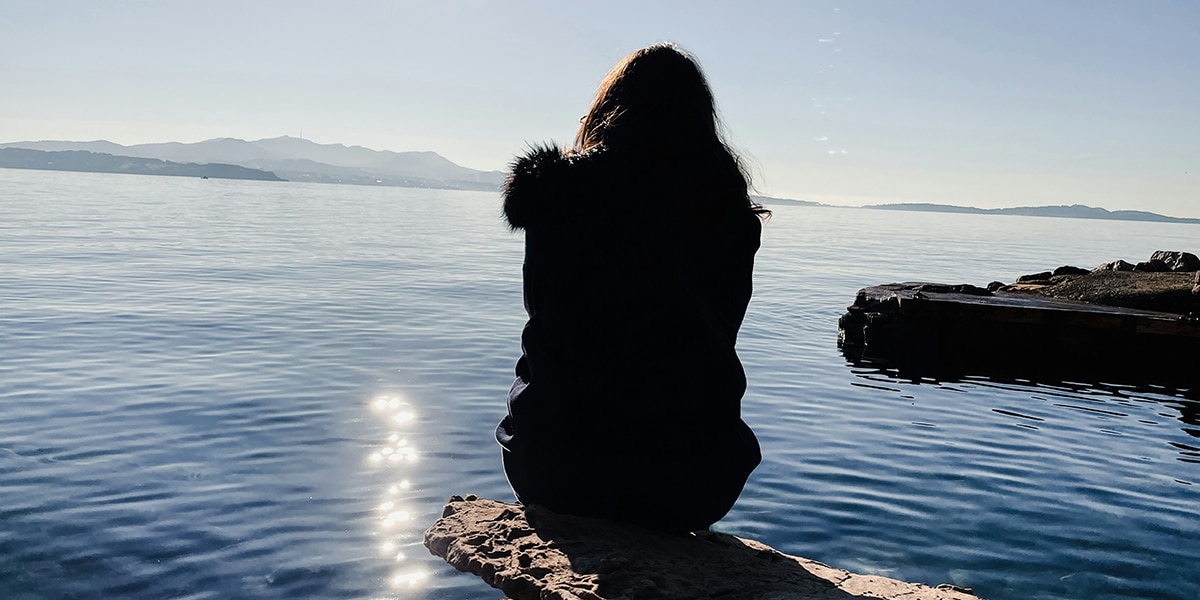 woman sitting and praying by a lake close to sunset