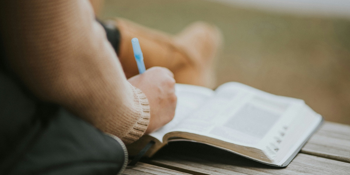 person writing down words while reading Bible