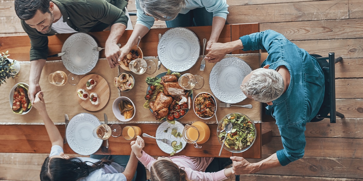 family holding hands around the dinner table while praying.