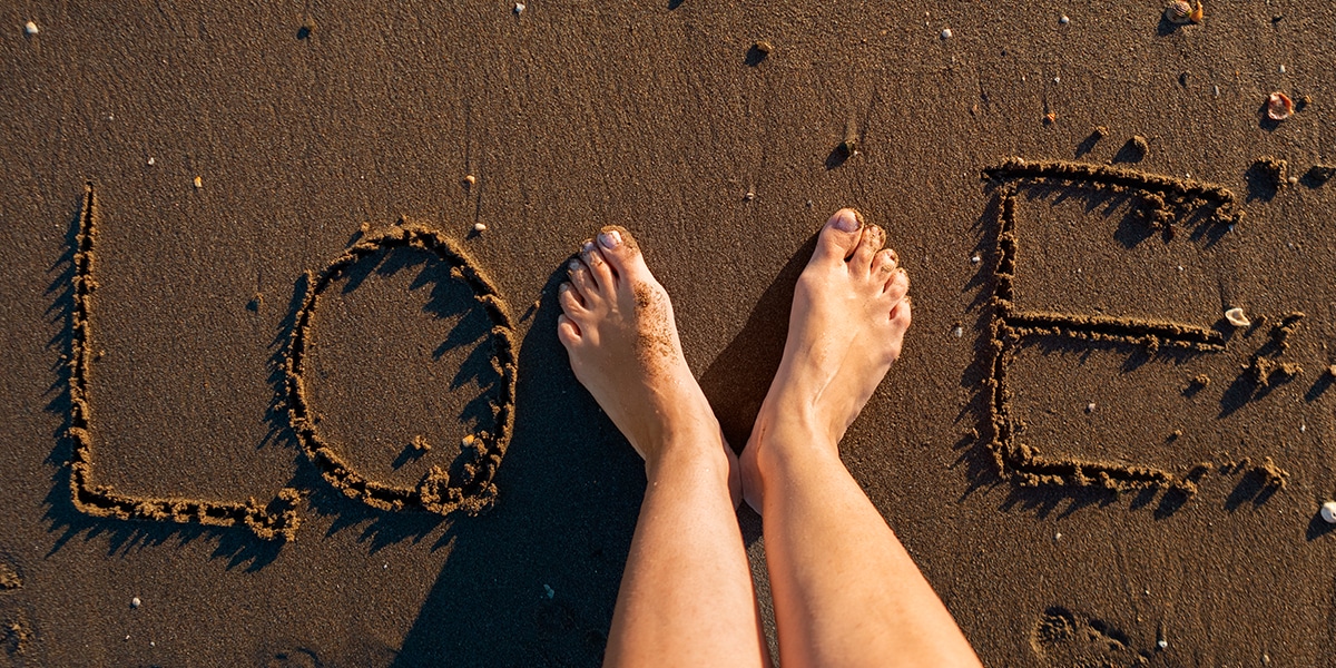 The word LOVE written in sand with two feet forming the V