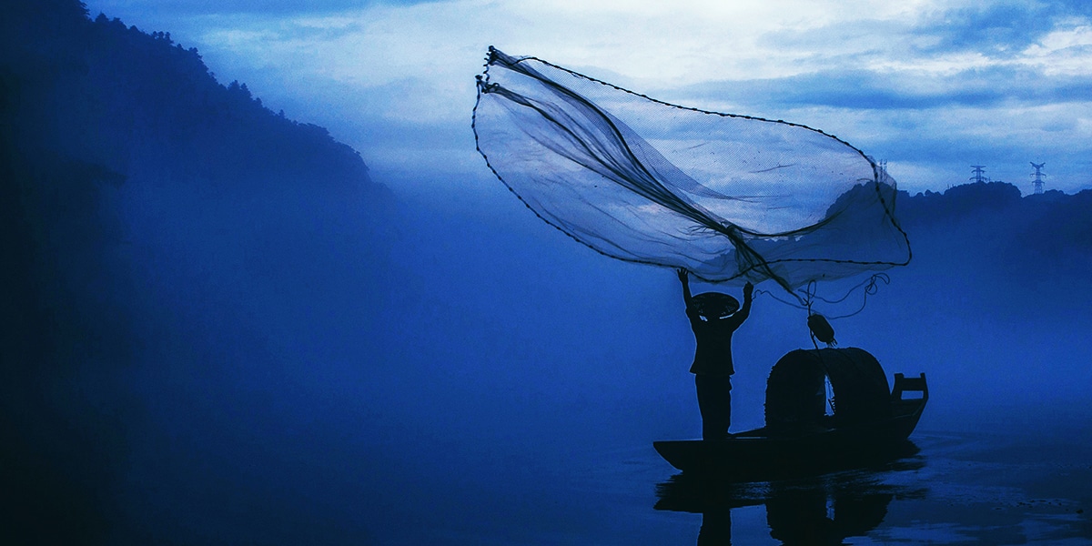 a fisherman throwing out a net into the ocean.