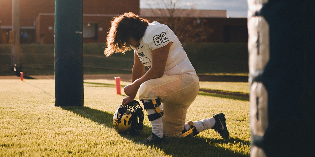 A young football player, kneeling in prayer before the game.