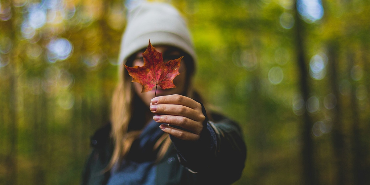 woman holding a leaf in front of a forest