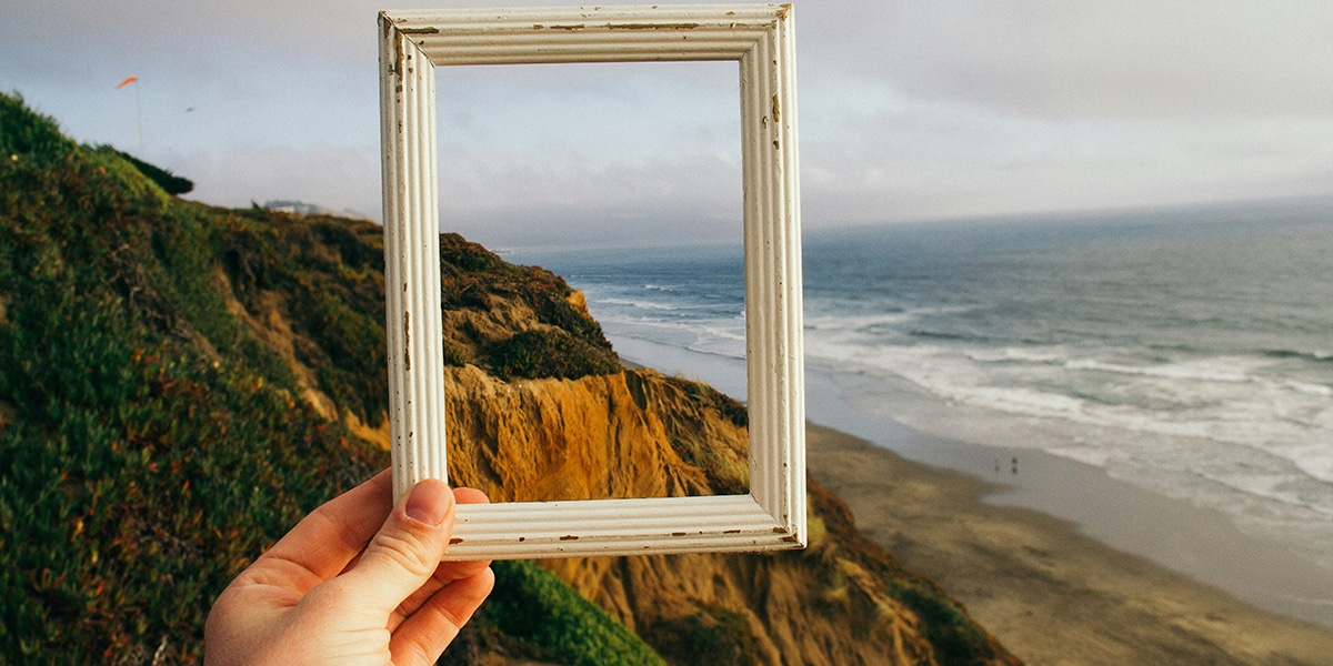 Hand holding a picture frame, framing in nature in the background.