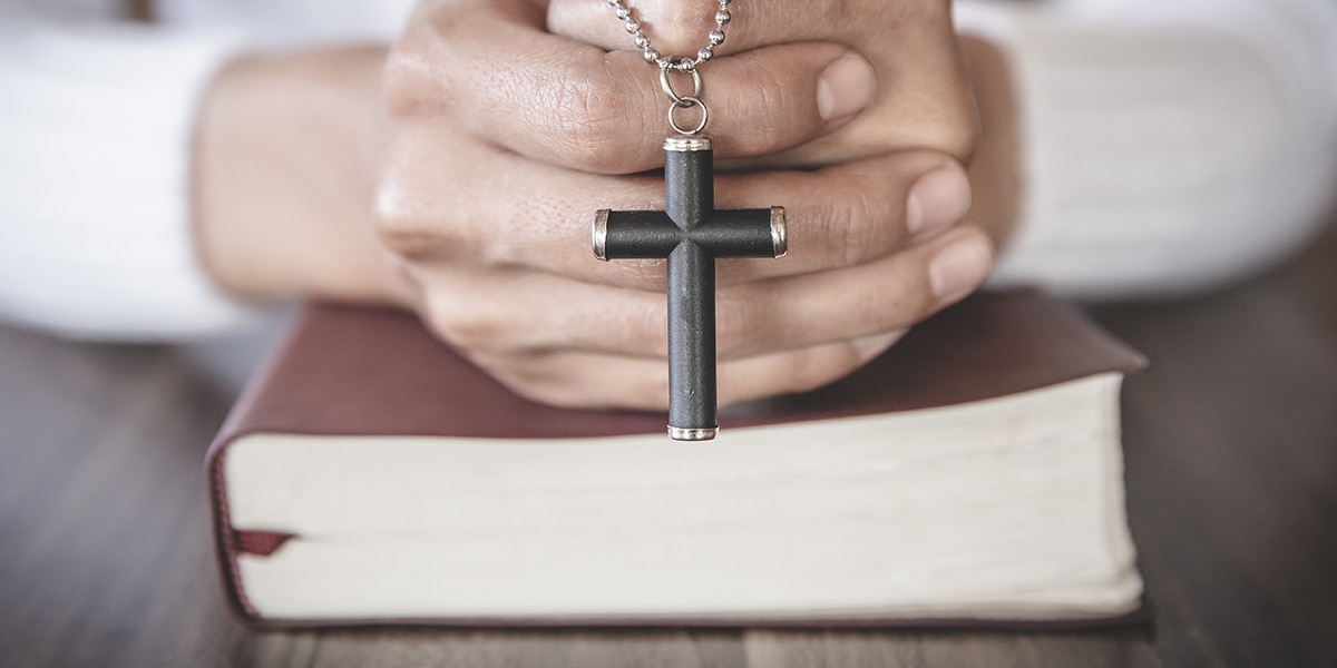 hands folded over a Bible holding a cross