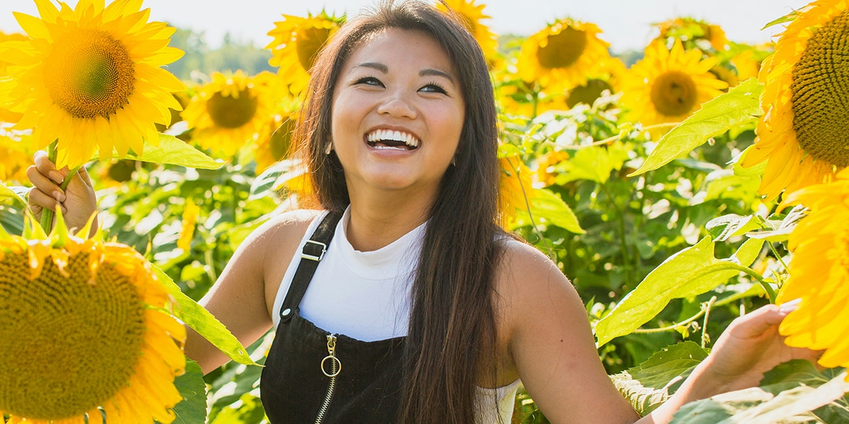 woman joyfully looking into sky while standing in a sunflower field.