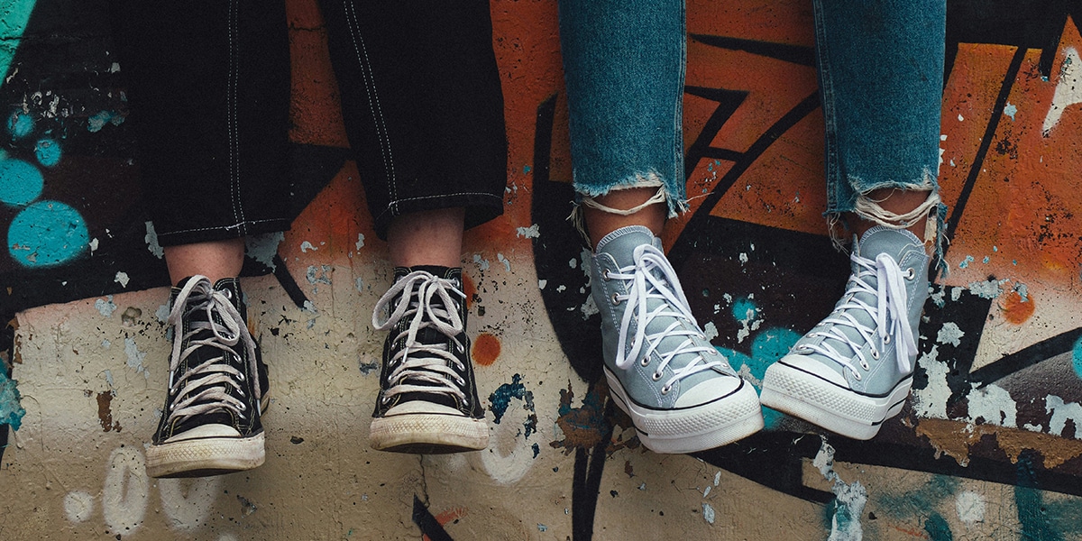 two kids wearing sneakers, sitting on top of a graffiti wall