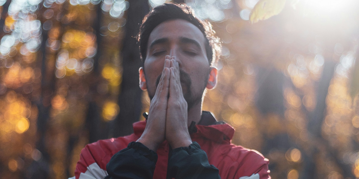 man reflecting with, taking a deep breath with hands folded.