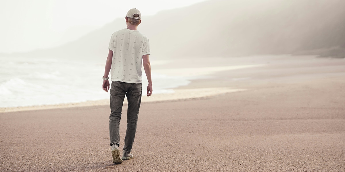 man walking along beach on the ocean with cliffs in the background.