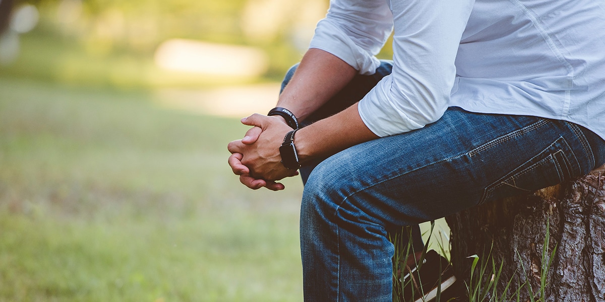 man praying with his hands folded while sitting on a tree stump.