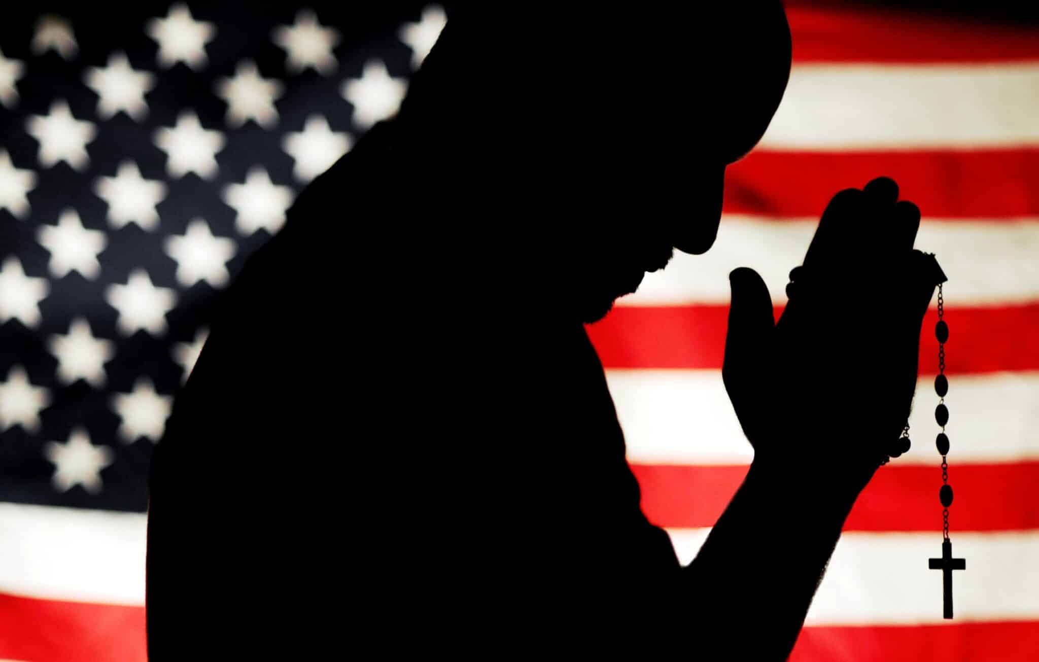 A man is pictured holding a rosary with the U.S. flag as a backdrop is silhouetted in this photo illustration.