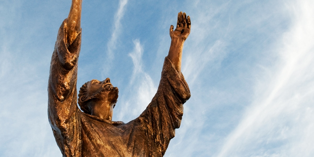 A statue of St. Francis with raised hands and looking into the sky