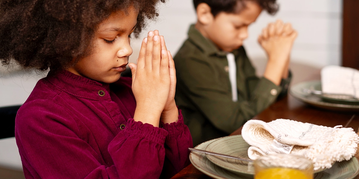 Two kids praying with folded hands before meal