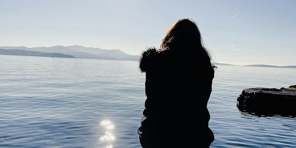 Woman sitting by a peaceful lake with the sunlight reflecting.