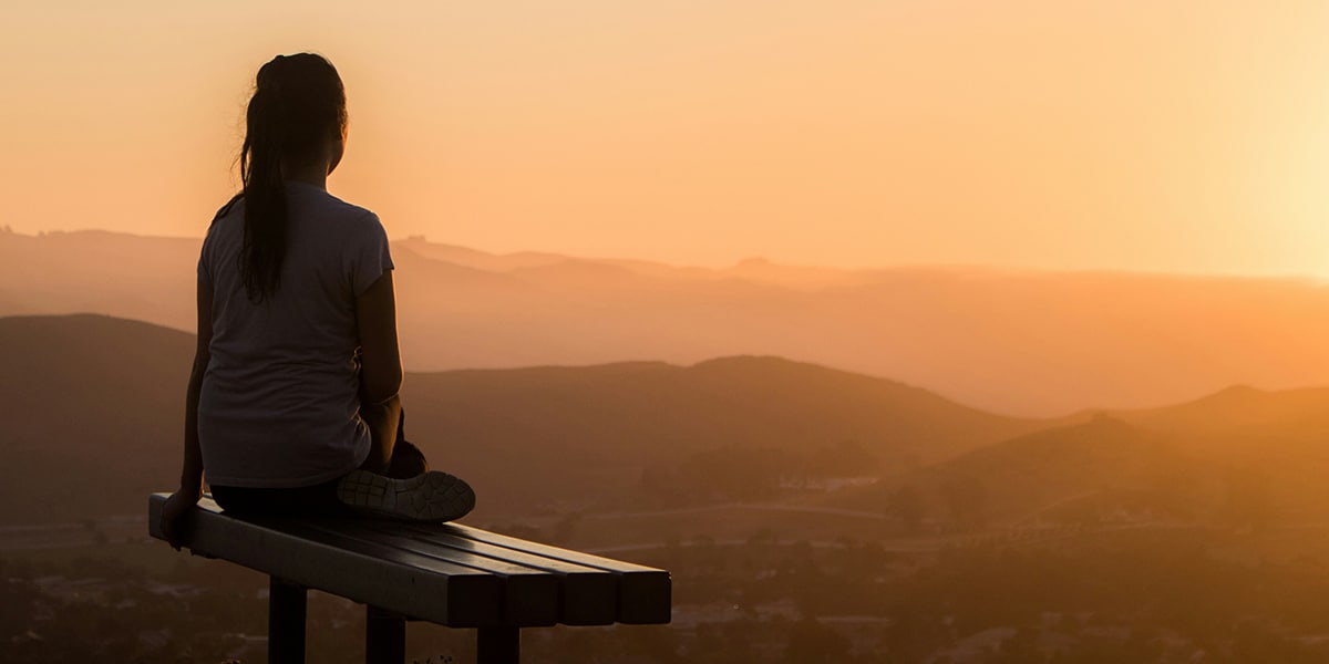 woman sitting on a bench in solitude watching a sunrise.