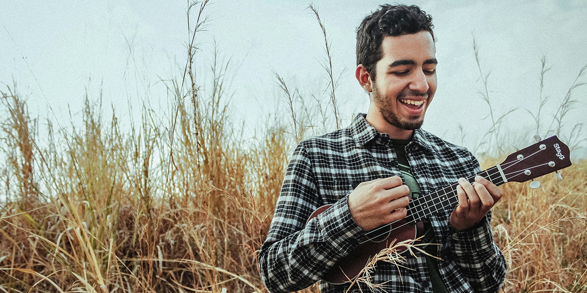 Happy musician plays the ukulele in a field