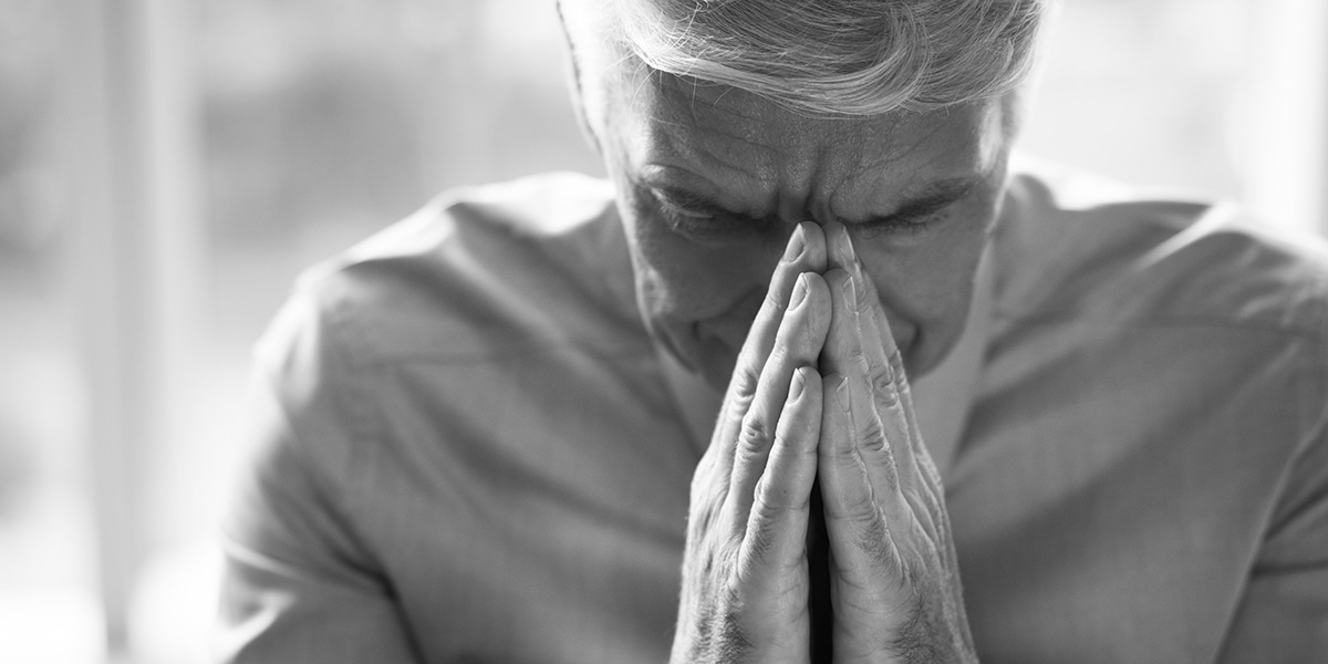 a older man praying with hands folded.