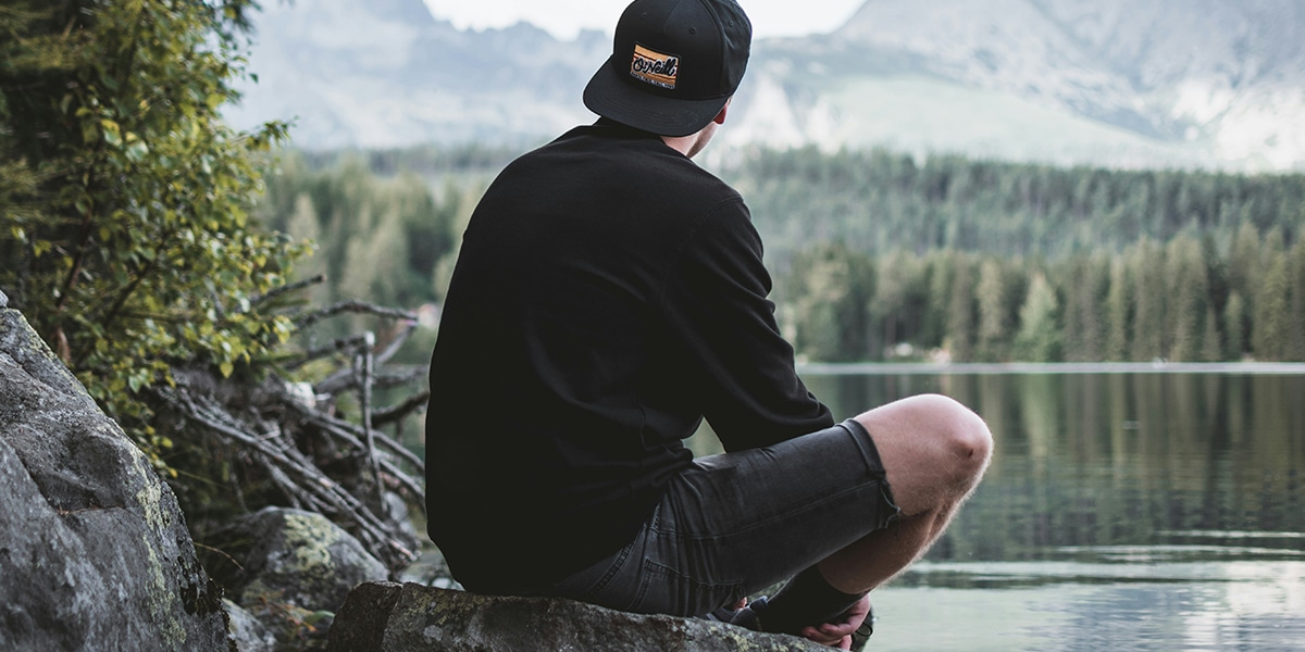 man sitting quietly on a rock by a lake.