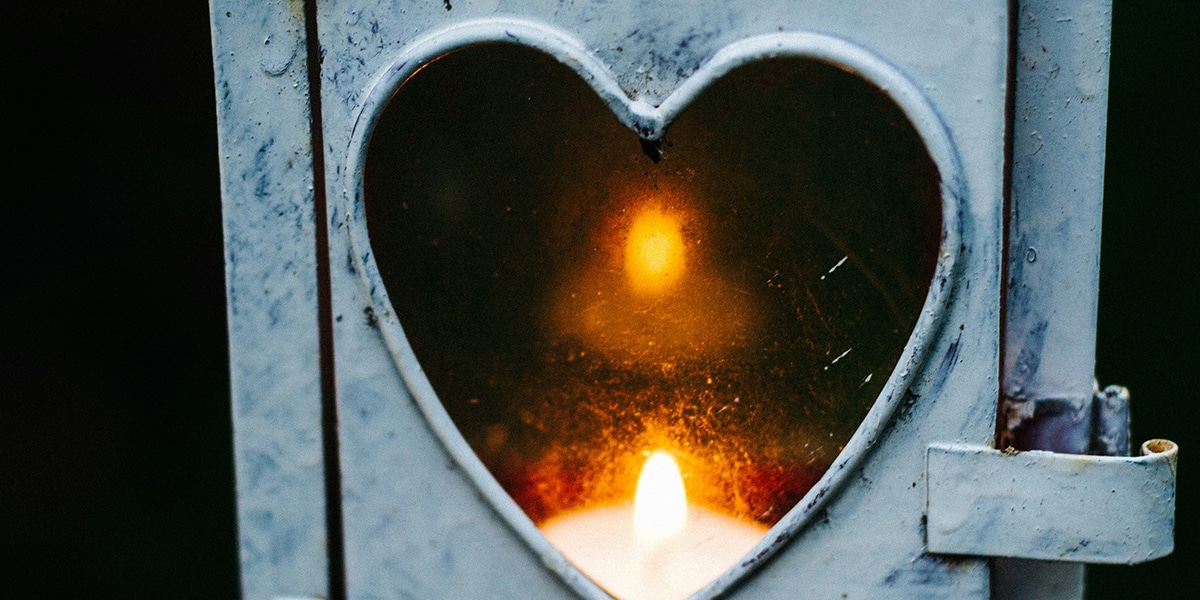 A lantern wot a heart shape glass showing the flame of a burning candle