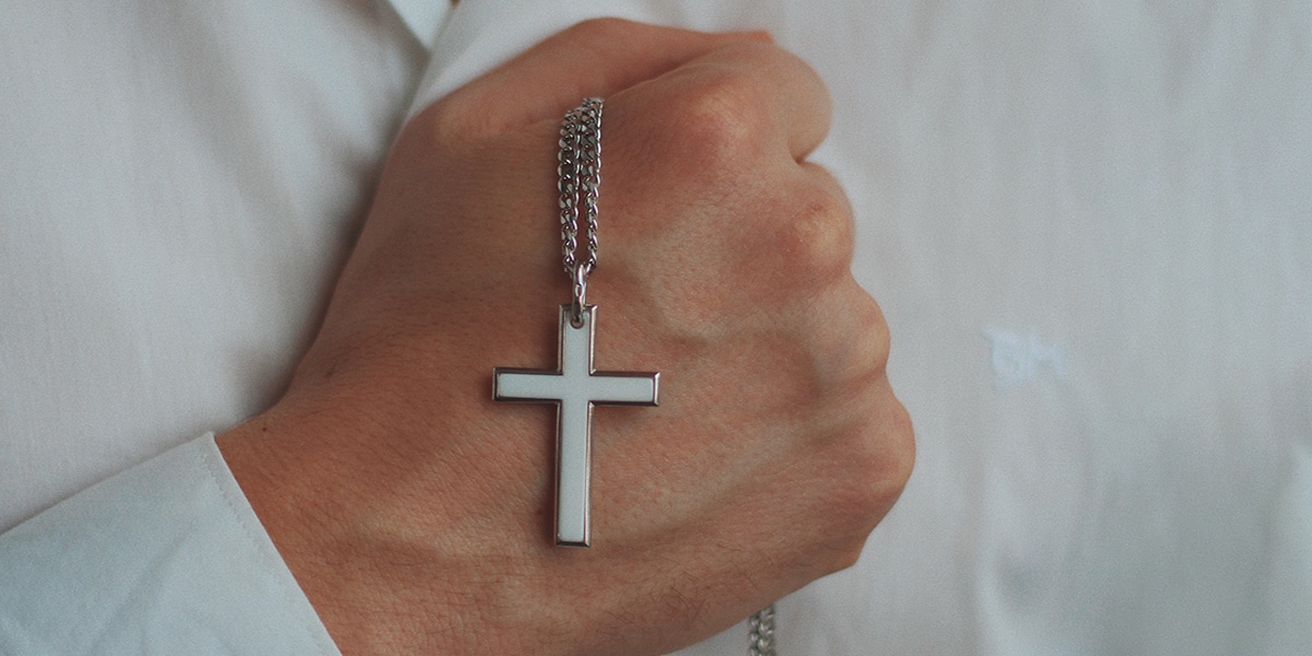 person making a fist with hand, holding on to a cross necklace