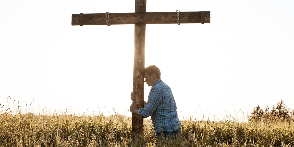 man leaning against a cross in a field.