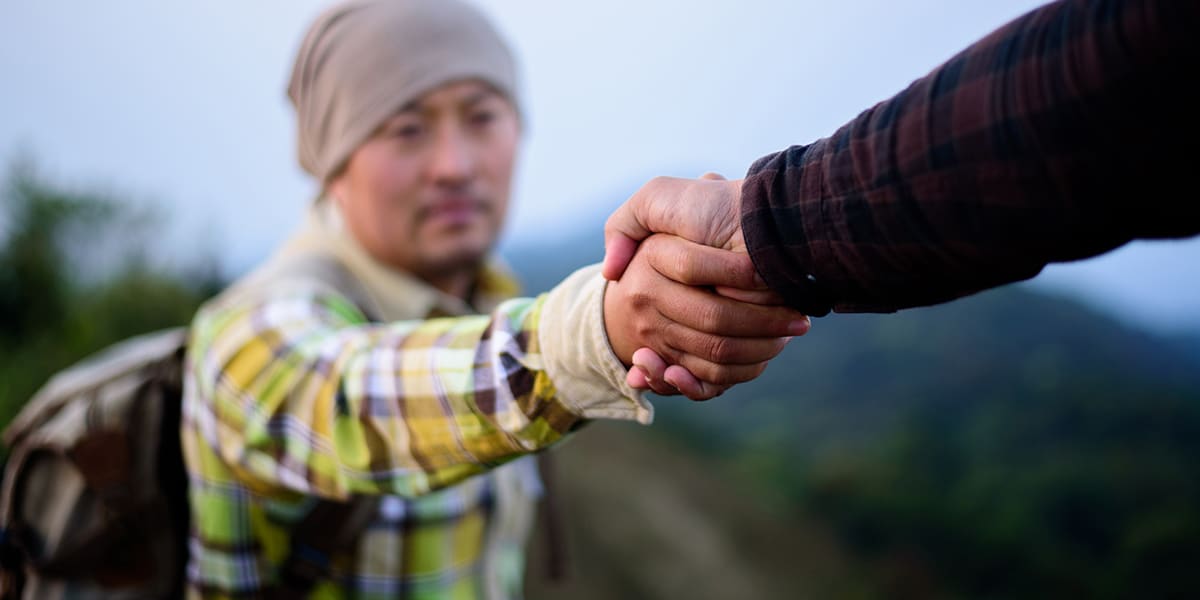 person reaching out a hand to help pull a man up.