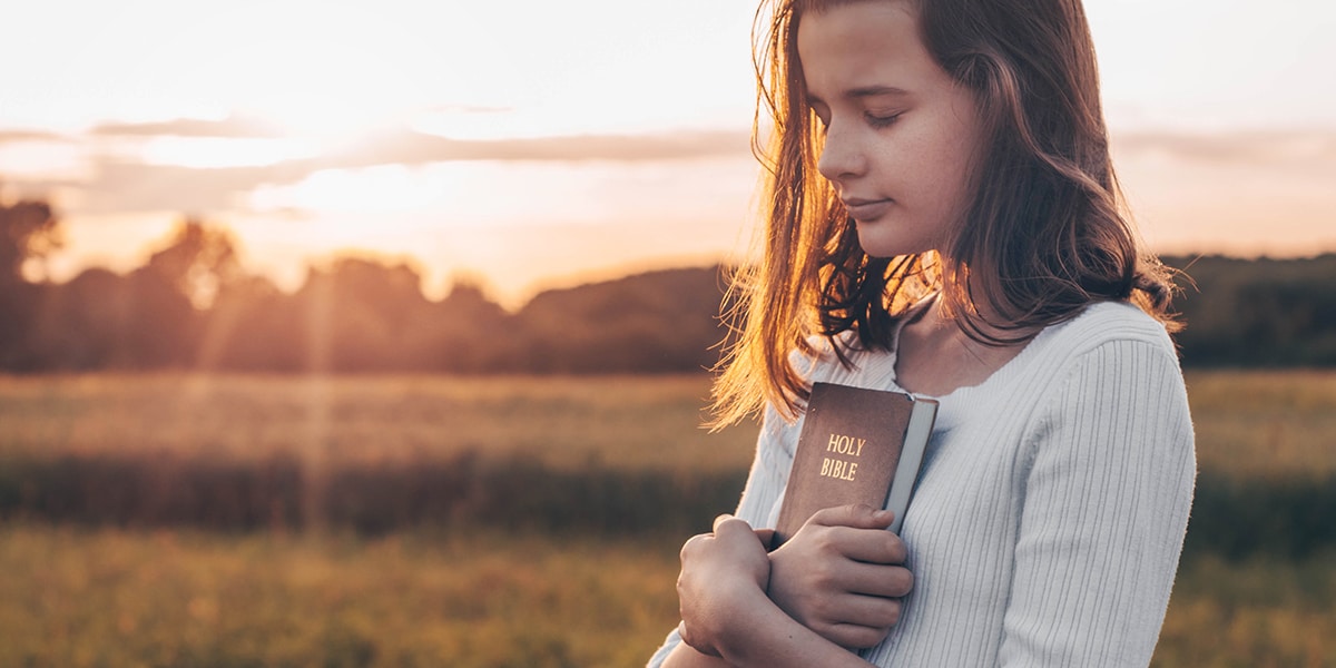 teenager reflecting on the Word of God while holding her Bible