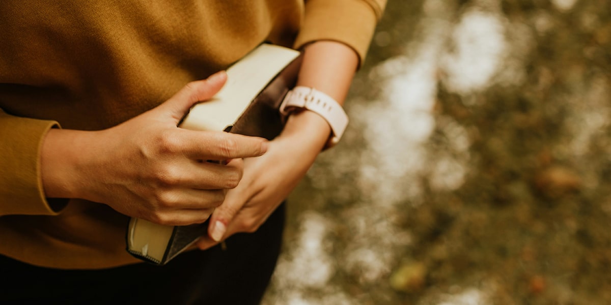 woman holding a Bible in her hands, close to her body.