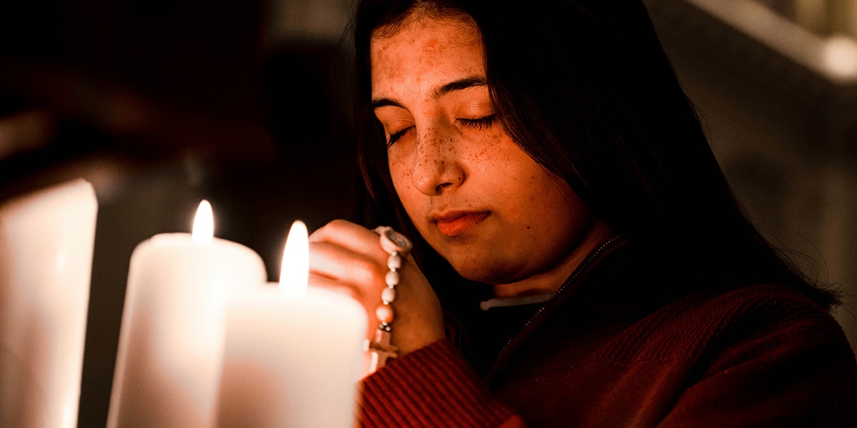 young woman praying surrounded by candles