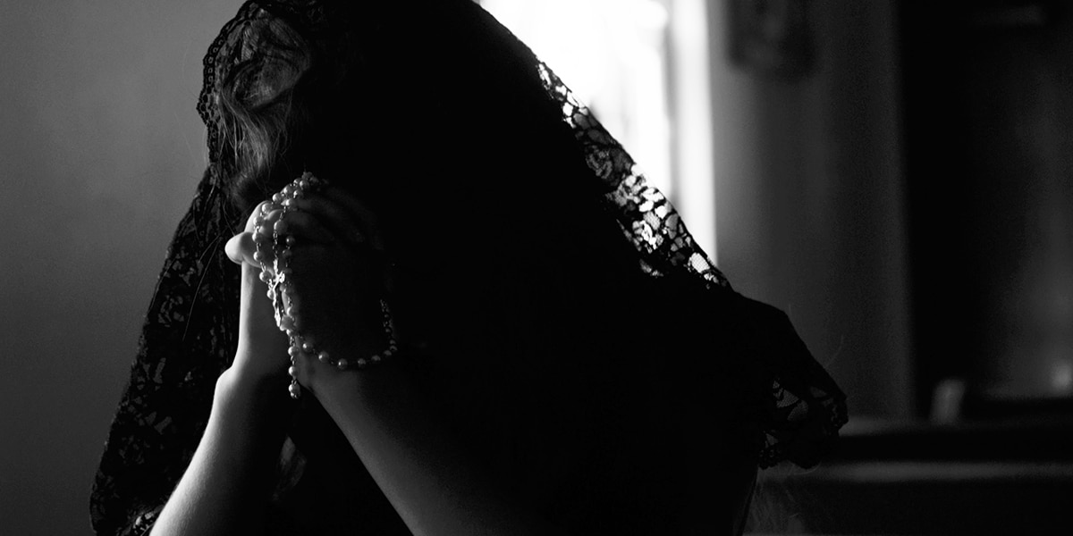 woman praying in a church holding a rosary and covering her head.