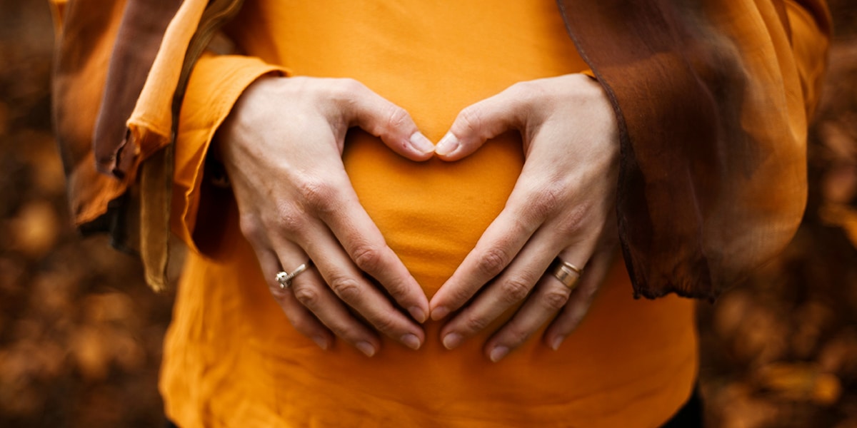 woman holding her hands in front of her womb, forming a heart