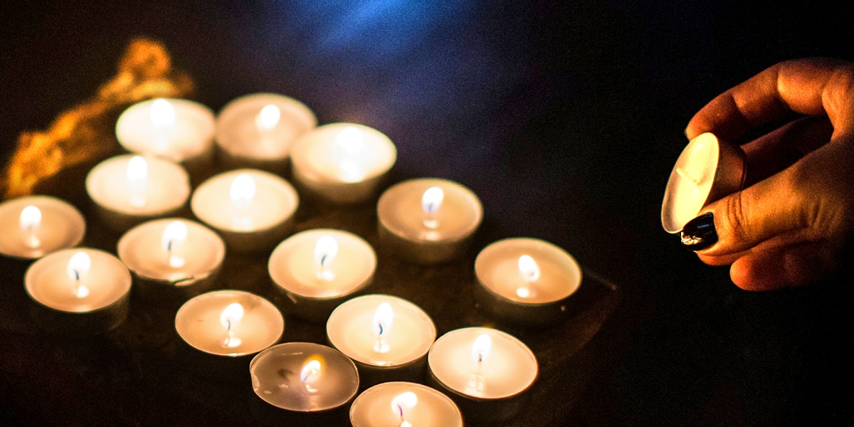 A hand is holding a candle towards a bunch of lit up candles in a dark room