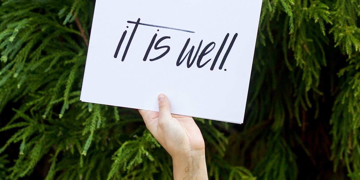 hand is holding a sign with the words "It Is well"