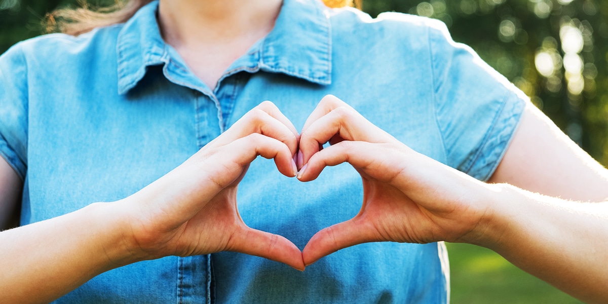 two hands are forming a heart in front of the person's chest.