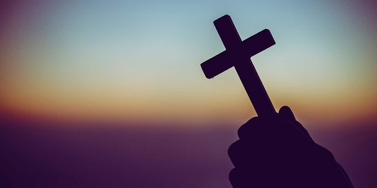 hands holding a cross with a sunset in the background