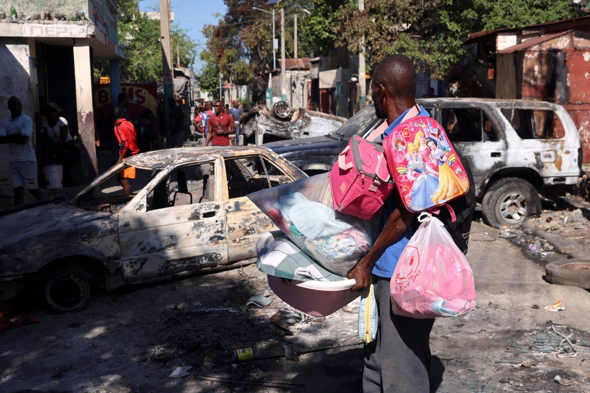 A man carrying his belongings observes the wreckage of vehicles burned by armed gangs as he flees the Poste Marchand suburb in Port-au-Prince, Haiti.